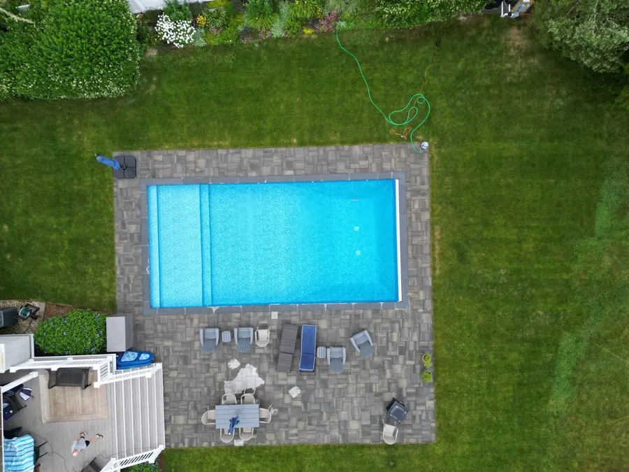 Aerial view of a rectangular pool and paver patio on a wide lawn