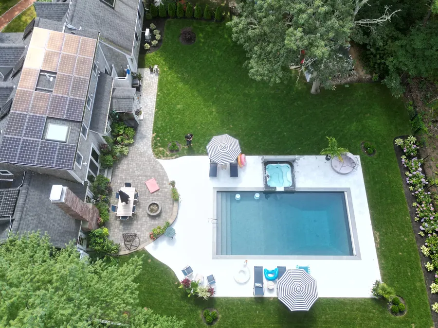 Aerial view of a pool with a hot tub and white patio