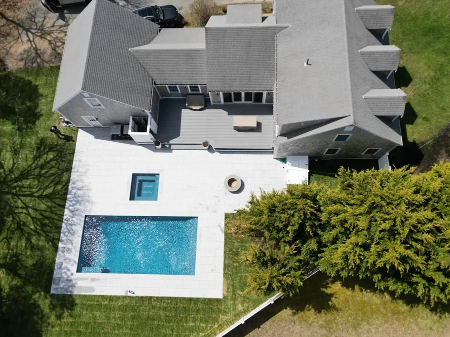 Aerial view of a pool, spa and fire pit behind a grey shingled house